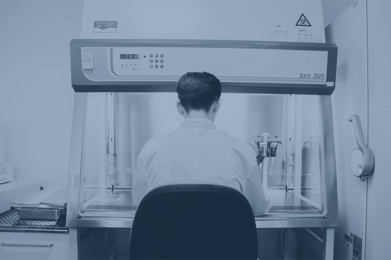 CatSci Bioscience Service: blue-toned image of male scientist in front of a glovebox in a lab
